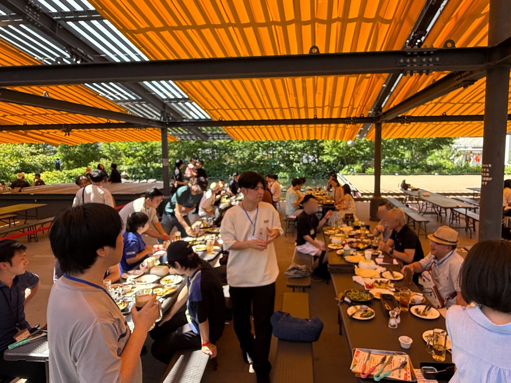 日本橋のテラス会場で、長テーブルを囲んで食事をしながら歓談する参加者