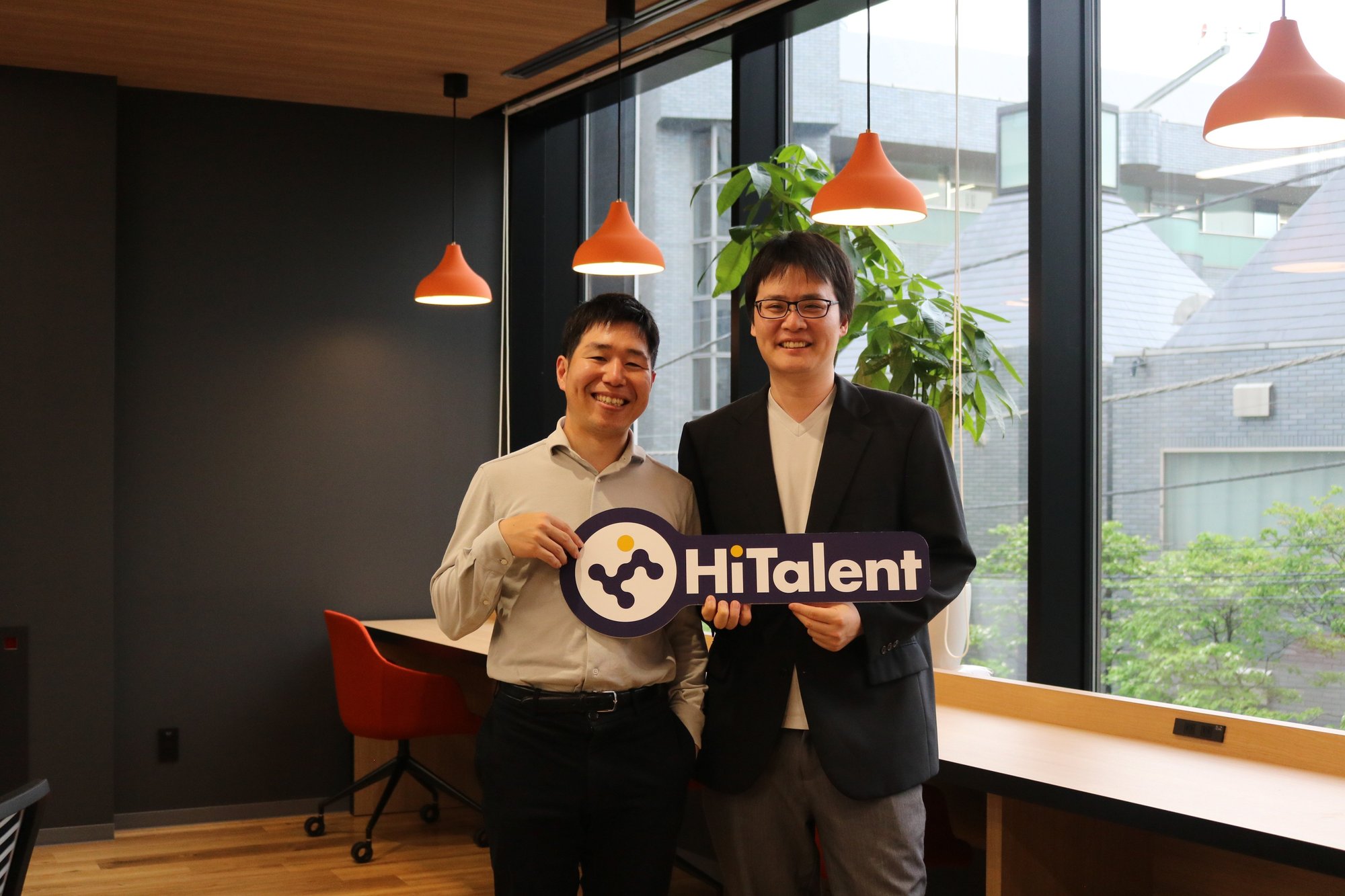 HiTalentのロゴボードを持って弊社メンバーと並ぶAさん