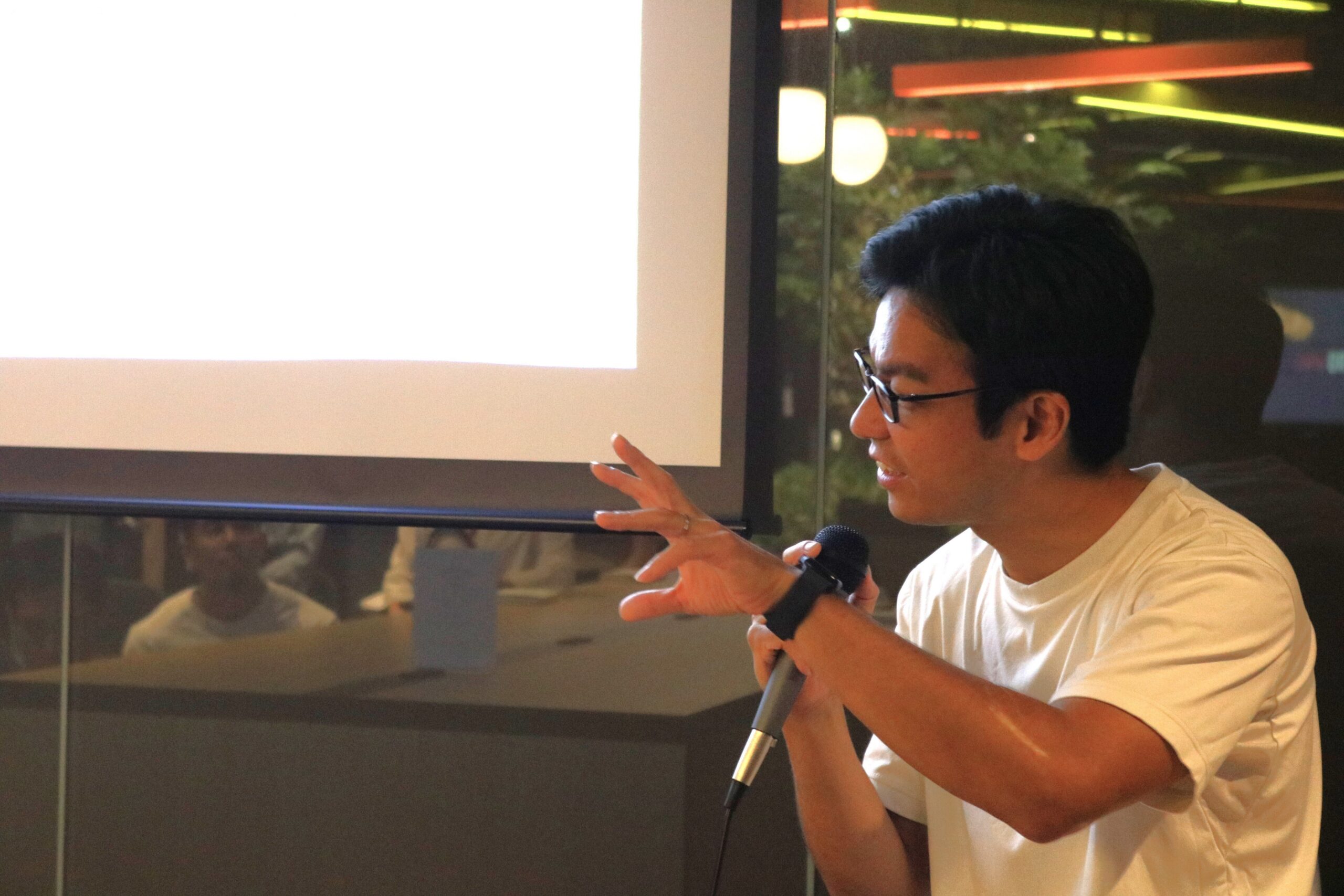 スクリーンを背に、マイクを手に手ぶりを交えて話す様子