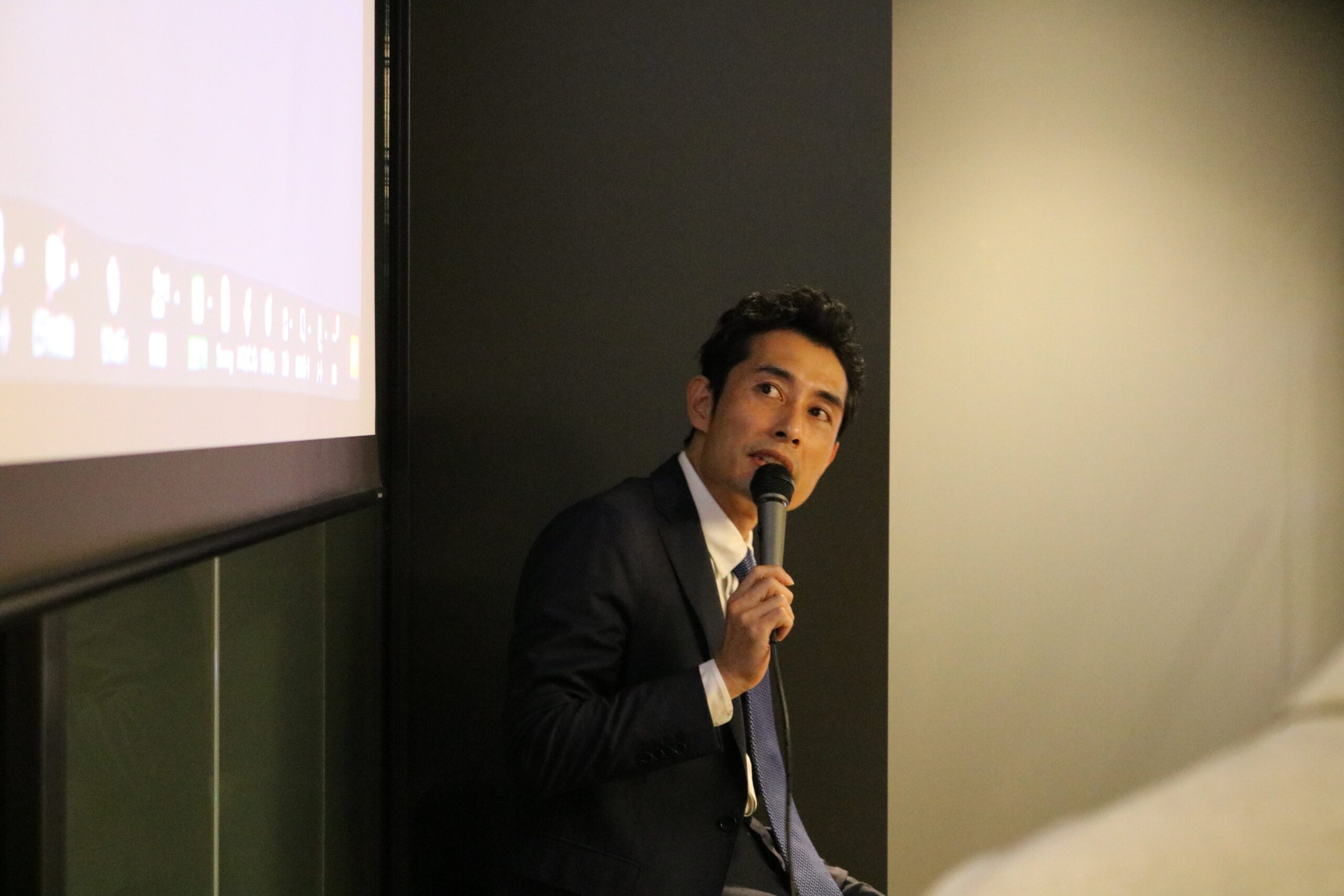 スクリーンを背に、マイクを持って講演する戸部克弘氏